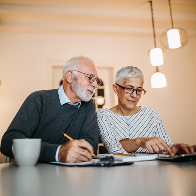 An older man with greying hair, holding a paper in front of his laptop deep in thought. He is holding his glasses in his right hand while resting them on his chin.