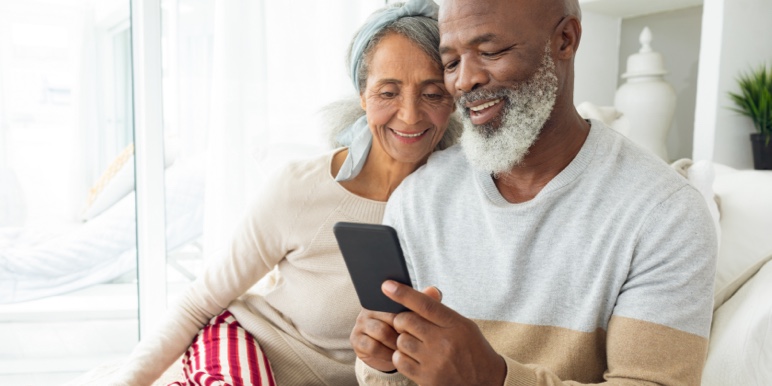 A retired couple sitting on their couch in their home nominating beneficiaries on their cell phone.