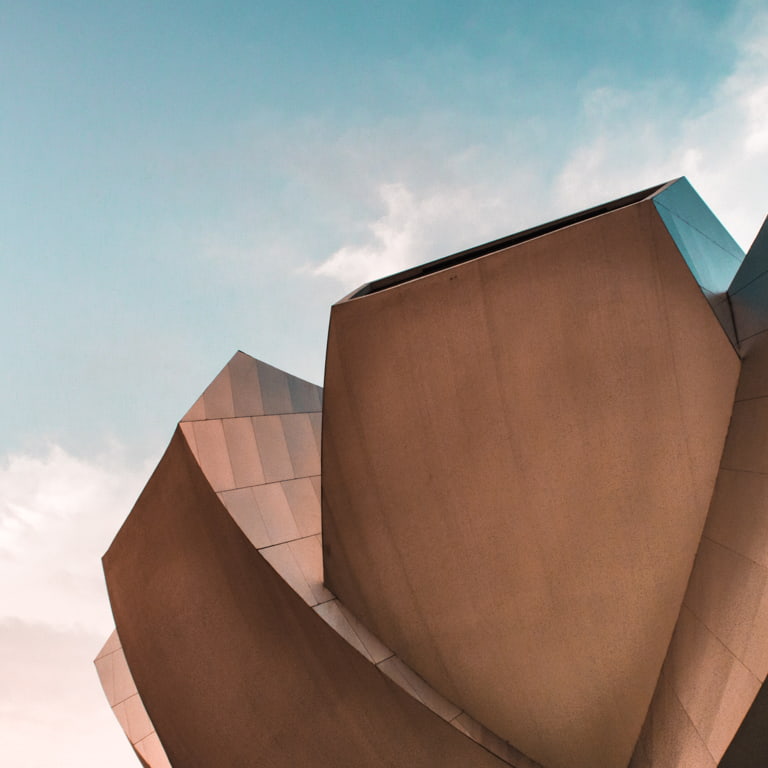 Foreground of a building showing cutting-edge modern design in the shape of a flower with a bright, blue sky in the background. 