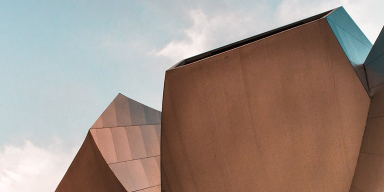 Foreground of a building showing cutting-edge modern design in the shape of a flower with a bright, blue sky in the background. 