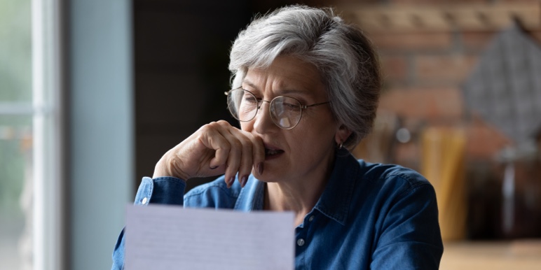A mature women sitting alone looking worried as she reads a document.