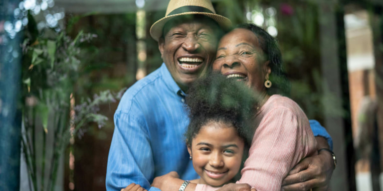 An old man and woman with big smiles, hugging their granddaughter.
