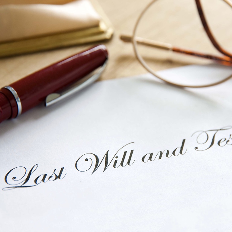 A piece of paper with a pen and eyeglasses on it and the words ‘Last will and testament’ written.