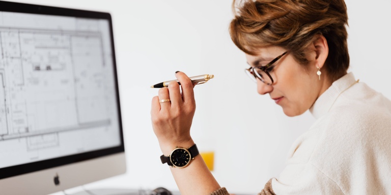 A business owner looking at a floor plan of her business premises on her computer, holding a pen in her left hand, considering some options to expand the business.
