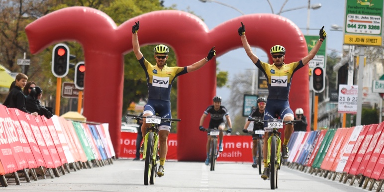 Two mountain bike cyclists in rugged terrain cycle past a vast mountainous area on the Merino Monster climb.