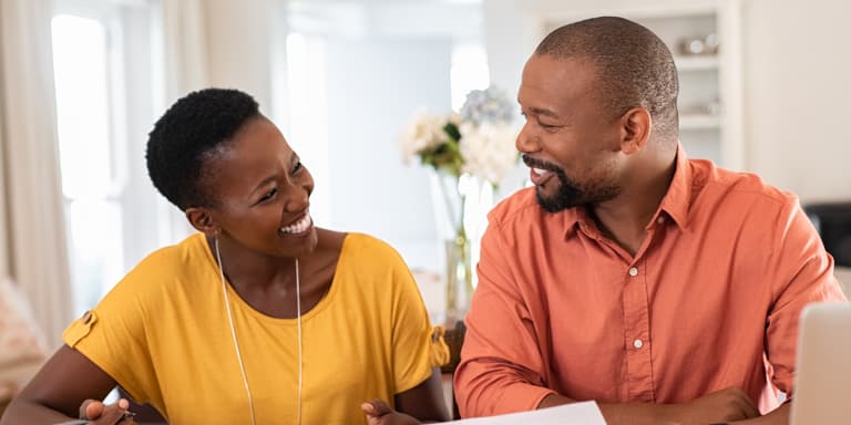A husband and wife look at each other smiling while reviewing their tax and retirement and investment goals.