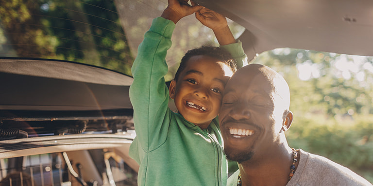 Closeup of elated father and son in the back of an open car boot. The father has just learned about Momentum Insure’s Safety Returns rewards program and related safety-focused features such as Safe DayzTM and Safety Alert.