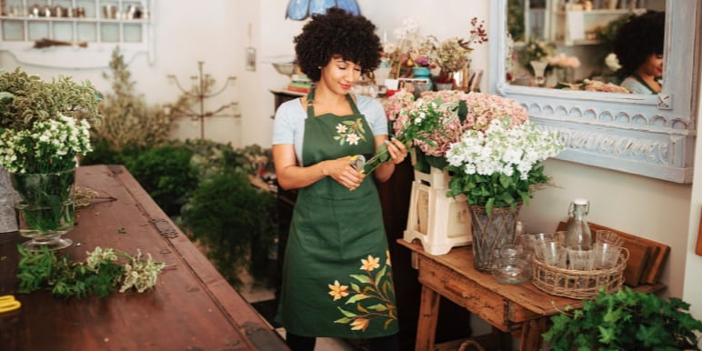 A florist standing cutting flowers in a flower shop.