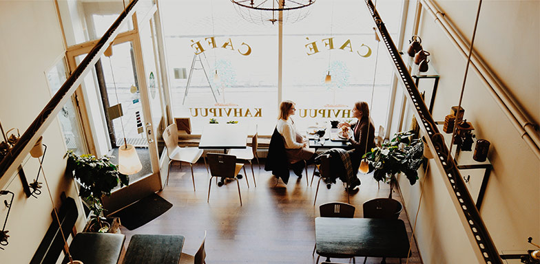 A modern café with large windows, wooden furniture, and people working at tables. Ideal for businesses looking to protect their building and assets with insurance.