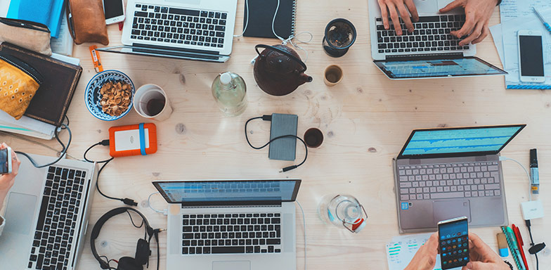 A top-down view of a shared workspace with laptops, keyboards, and coffee cups, highlighting the importance of electronic equipment insurance for small businesses in South Africa.