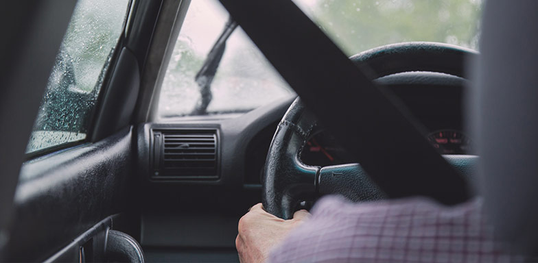A close-up of a driver’s hands on the wheel with a seatbelt fastened, symbolising protection against third-party claims covered by public liability insurance in South Africa.