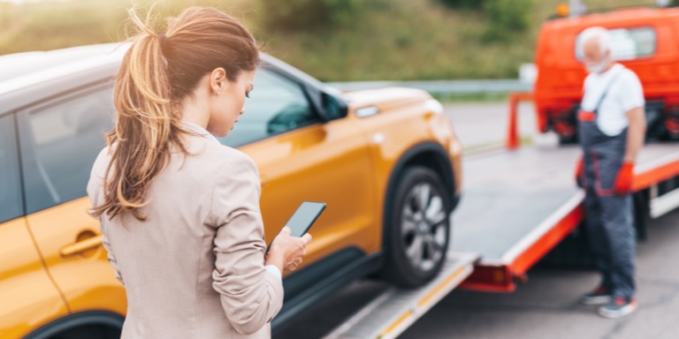A young lady on her cell phone standing alongside her car that is being towed. She has car insurance from Momentum Insure.