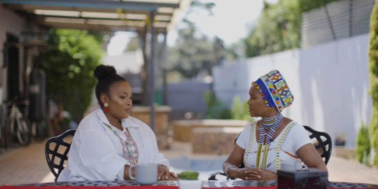 An image of Mam’ Noxolo Grootboom having a seated conversation with an interview outside, for the Coffee Conversations webcast.