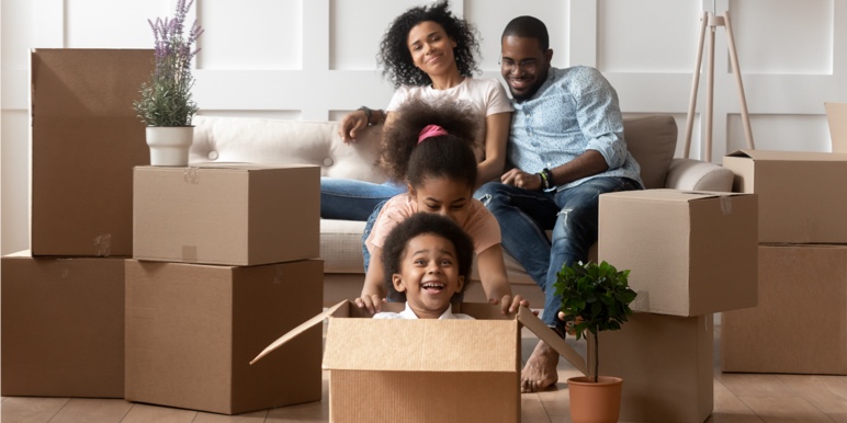 Family sitting amongst boxes in a new house with the children playing in the boxes.