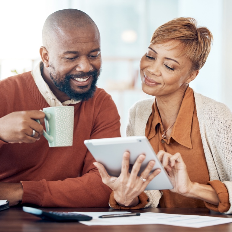 A middle aged couple sitting at the table comparing retirement annuity options from a tablet