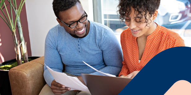 A young couple sitting on a couch, with a laptop at home planning their finances. 