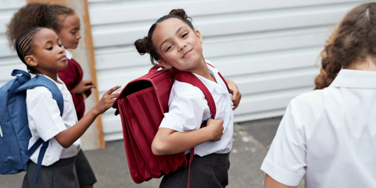 A little girl in her school uniform, satchel on her back, beams with joy as she heads to school, excited for a day of learning and new adventures.
