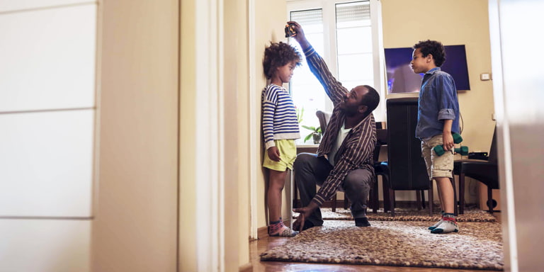A young dad measuring his youngest son's height while the elder son looks on.