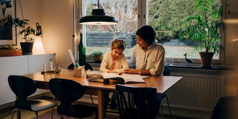 A mum and her daughter sitting at a table doing homework in the early parts of the evening.