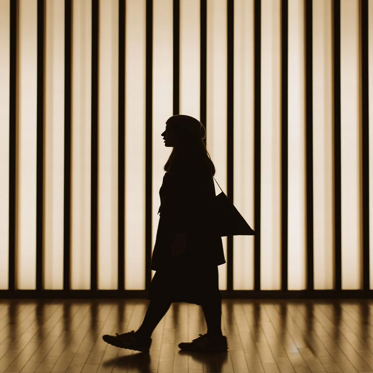 Silhouette of woman walking in front of striped illuminated wall.