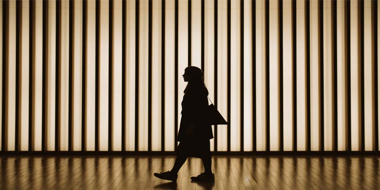 Silhouette of woman walking in front of striped illuminated wall.