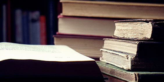 Old legal books stacked on a table. One book lies open on the table.