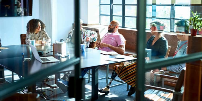 A middle-aged lady with a prosthetic limb sitting around a conference table in a meeting with her colleagues.