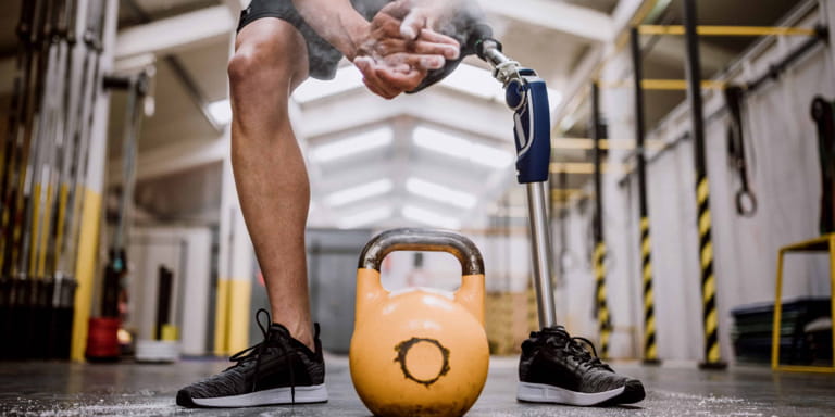 A male with a left prosthetic leg claps his hands to dust off the excess powder in preparation to pick up a heavy kettle bell weight.