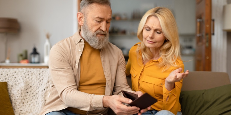 Mature couple sitting on a couch as the man shows the woman an empty wallet.