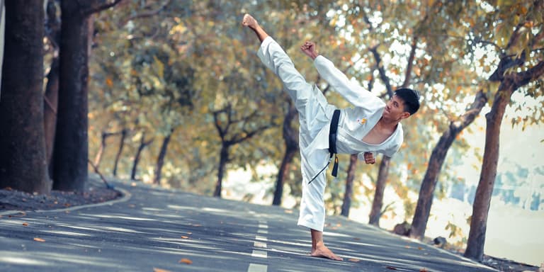 A man with a black belt in Karate training on a quite road.