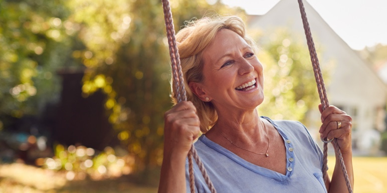 A retired woman sitting on a swing and smiling.