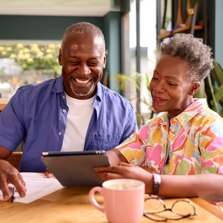 A happy, elderly couple sitting at the table reading their retirement annuity contracts on a tablet.