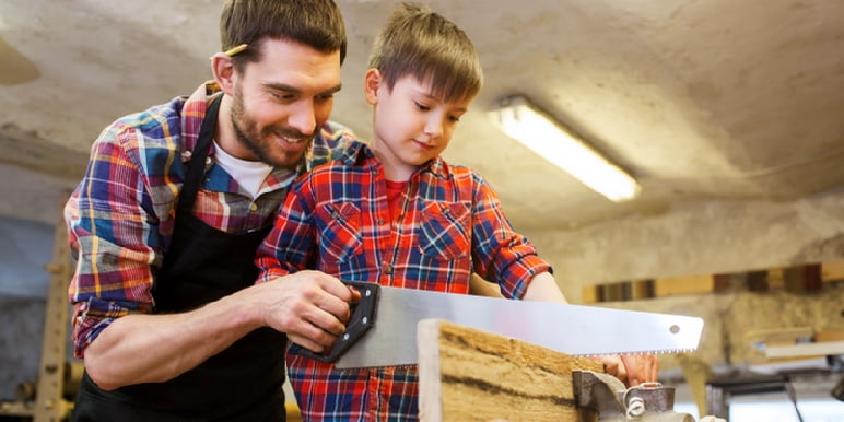 Father showing his son how to cut a piece of wood with a saw.