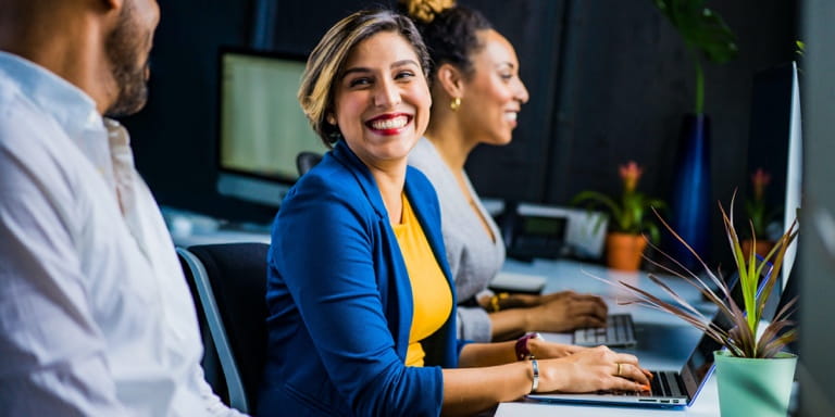 Three healthy individuals sitting at their workstations, chatting and enjoying their work.