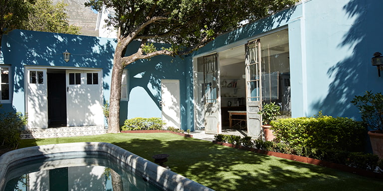 The outside of a blue house painted blue and white with a lawn and pool at the front.