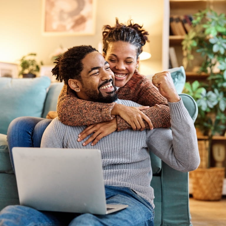 Happy young couple on a couch with a laptop, planning their legacy as part of the estate planning process.