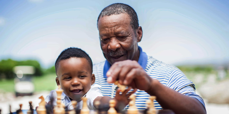 An old man enjoys retirement playing chess with his toddler grandson.