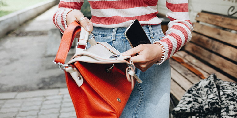 A woman opening her bag to place her cell phone inside. Momentum Insure has a handbag cover for females for handbag loss or theft and its contents.