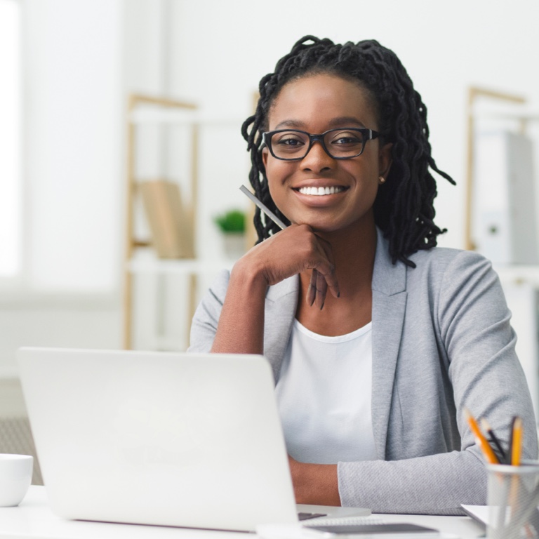 A happy, young female professional, at an office, sitting in front of a laptop.