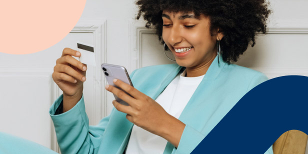 Young woman smiling while making an online payment using her phone and bank card, representing smart money management.