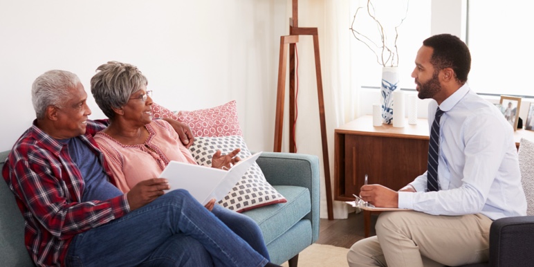 Financial adviser providing retirement benefit counselling to a couple nearing retirement, seated on their couch at home.