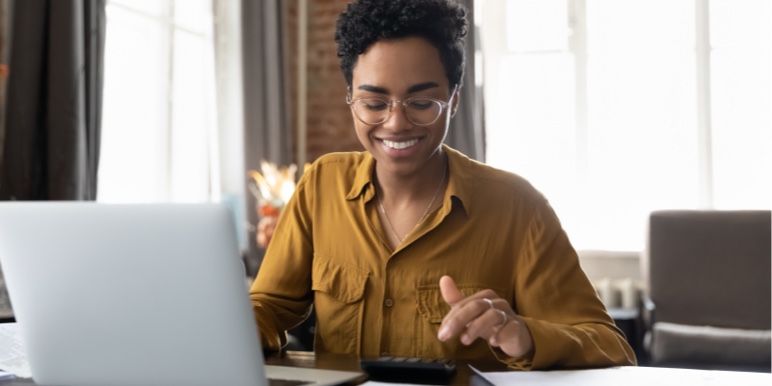 Young woman sitting and looking at her laptop while smiling.