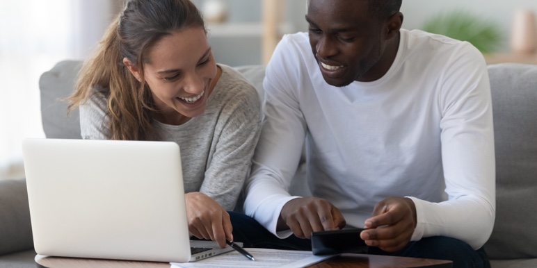 A couple sitting on the couch with a laptop and documents on the table in front of them.