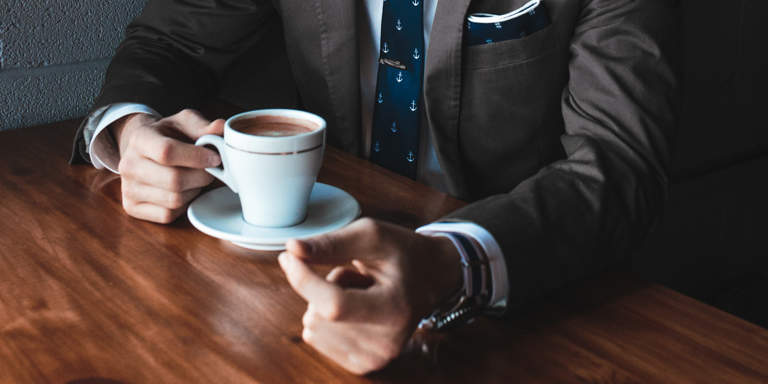 A man in a smart suit sitting at a table having coffee.