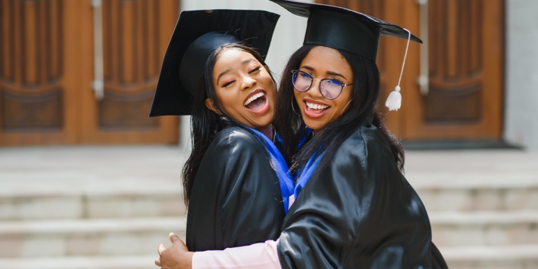 Two women graduates embracing each other while smiling.