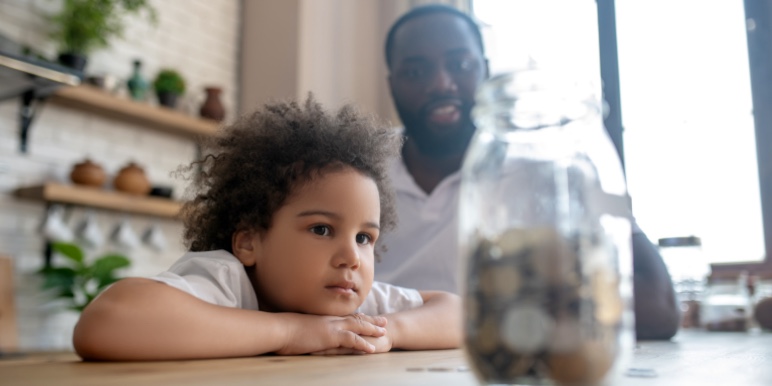 Son and father looking at jar full of coins.