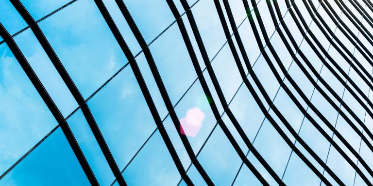 Low-angle perspective of a glass building with black lines.