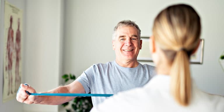 Senior man in physiotherapy session using resistance band at a Wellness Centre offering support for employees with illness or disability claims.