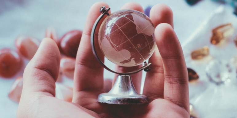 A hand holds a glass globe of the world.