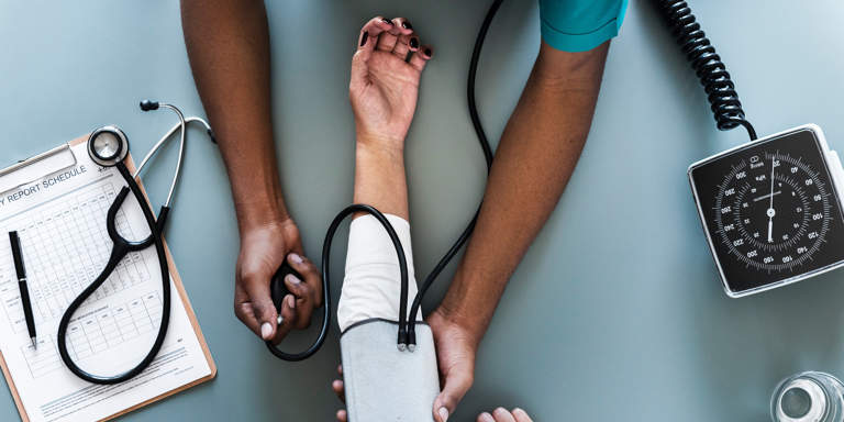 A nurse taking a patient’s blood pressure reading and noting it on the patient’s chart. 